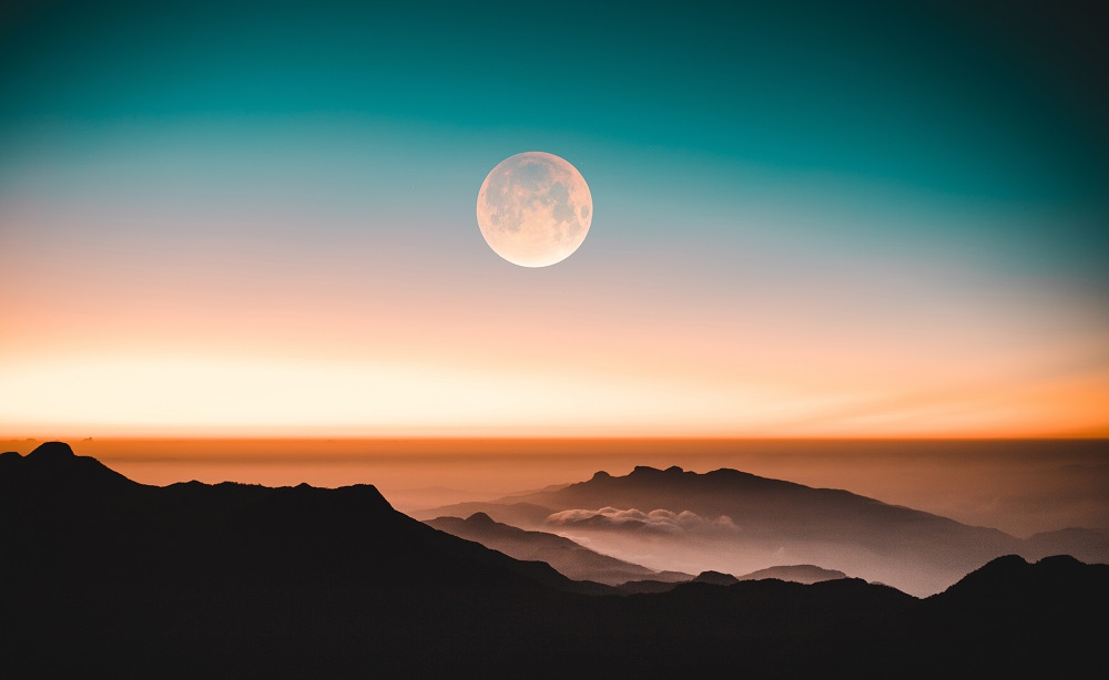 A goreous shot of the full mooon above cloud-covered mountains at sunrise. Looking at the effects of the full moon on your emotions 
